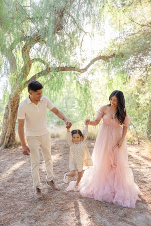 Family playing and dancing together under willow trees in matching white and pink outfits.