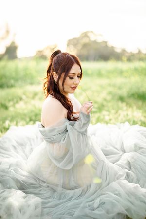 A person in an ethereal grey gown sits gracefully on billowing fabric in a spring meadow.