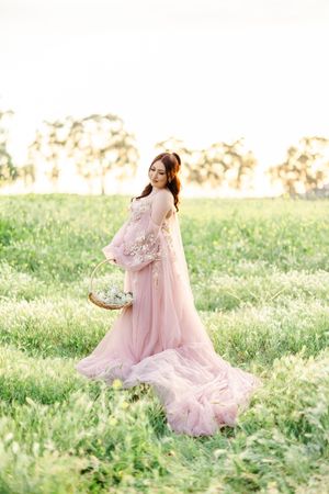 A person in a pink tulle gown poses in a sunlit meadow during golden hour.