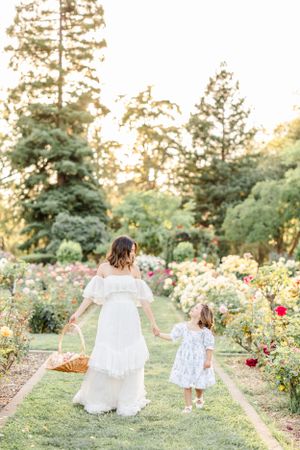 Mother and child walk through blooming rose garden paths at sunset.
