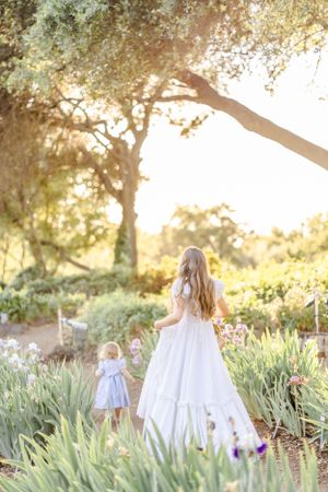 Ethereal garden scene with white-dressed figures walking among iris flowers at sunset.
