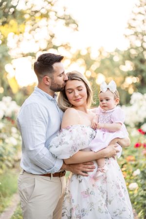 Family wearing coordinated white and floral outfits embrace in a garden setting at golden hour.