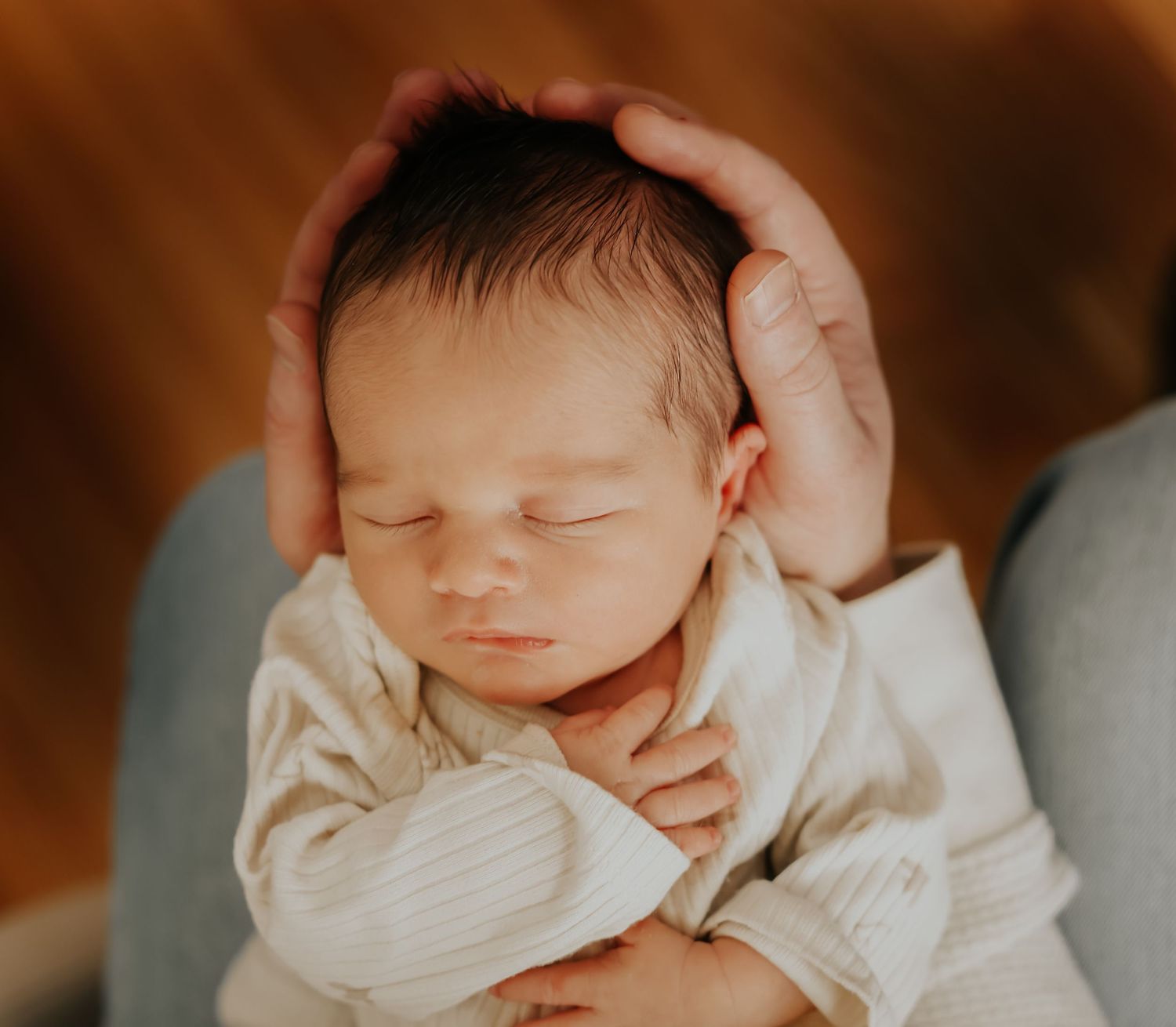 Peaceful sleeping newborn baby in white outfit being gently cradled by adult hand.