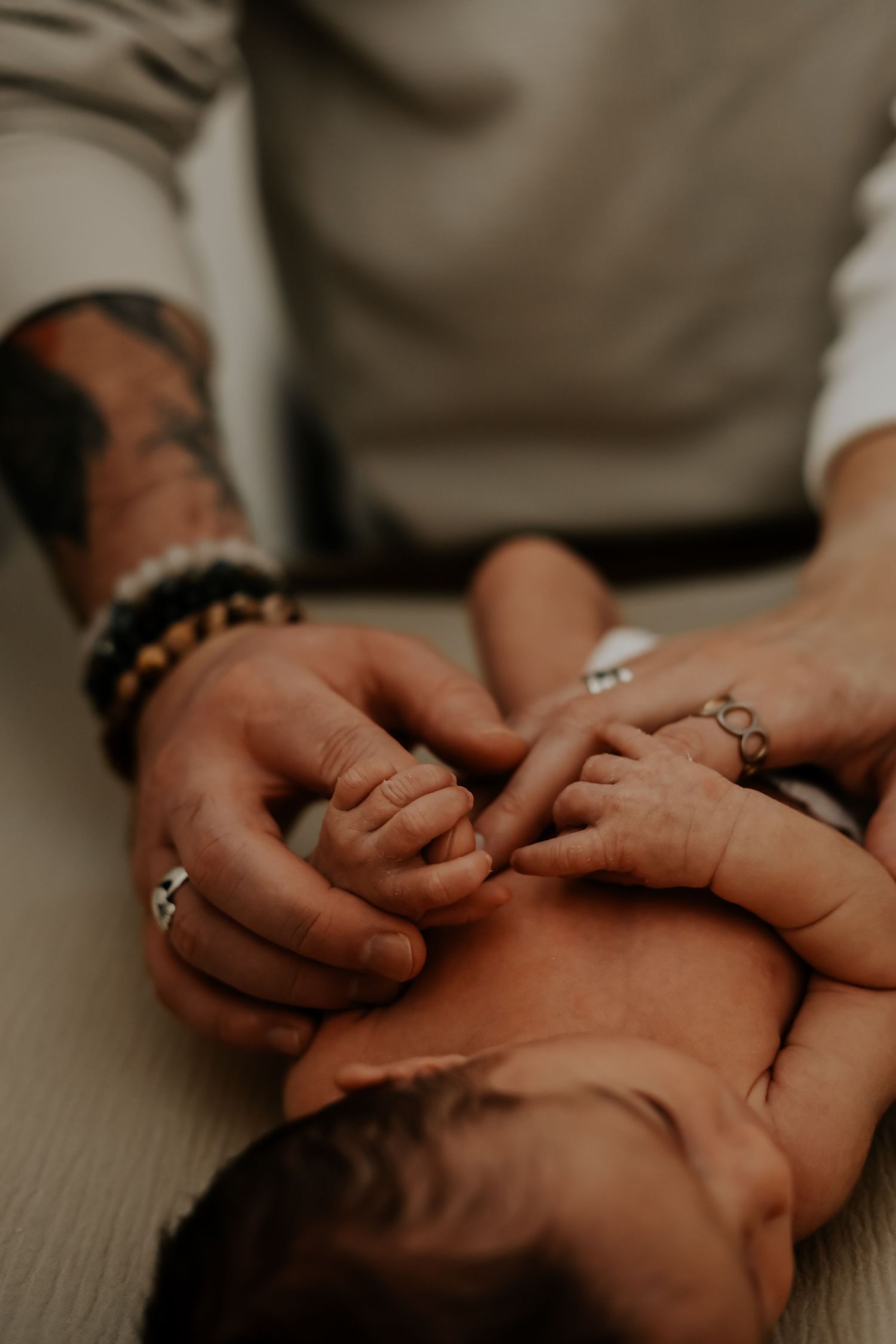 Close up of adult hands tenderly holding baby's hands with jewelry and bracelets visible.