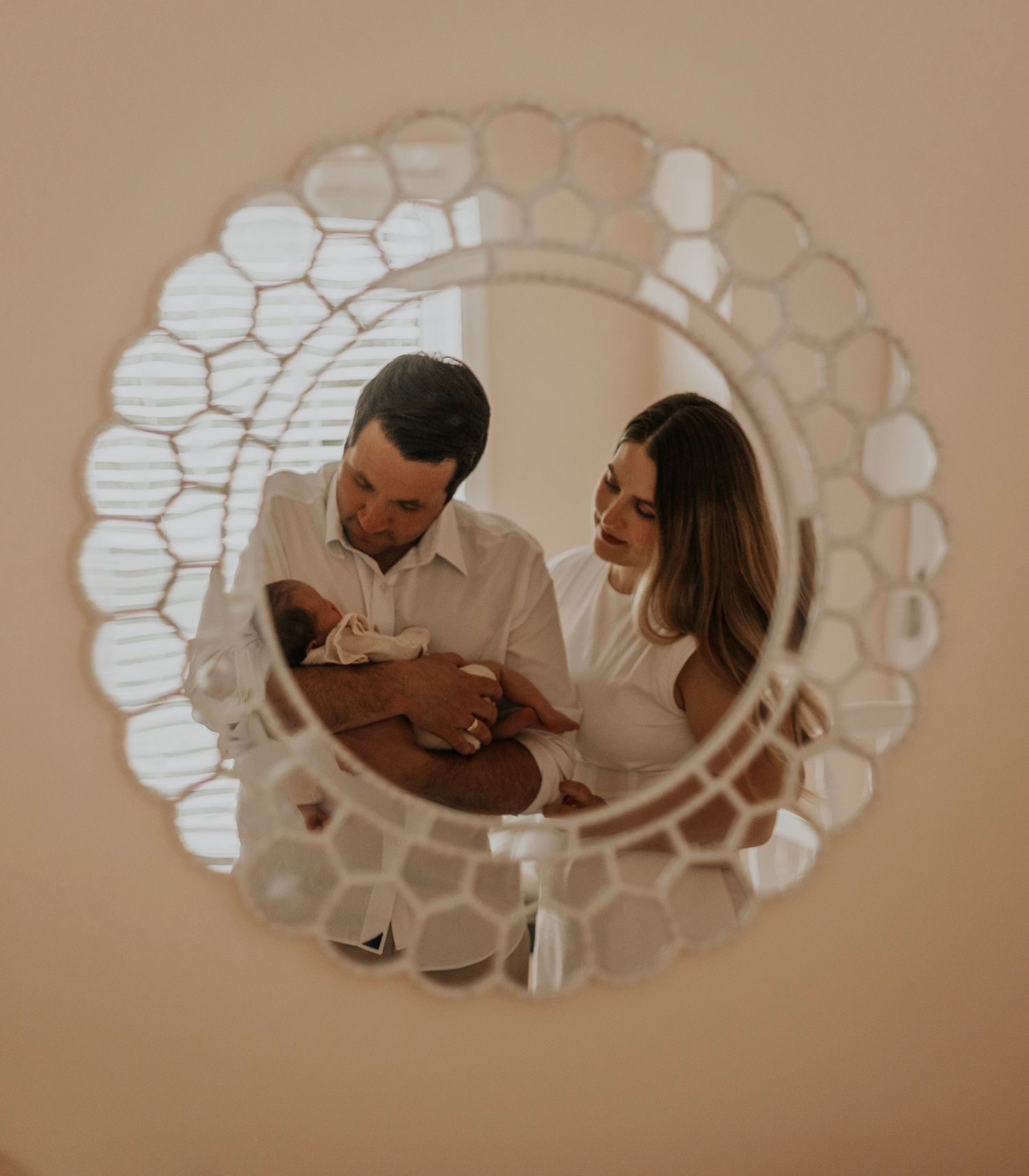 A reflection in a decorative mirror shows parents gazing at their newborn baby.