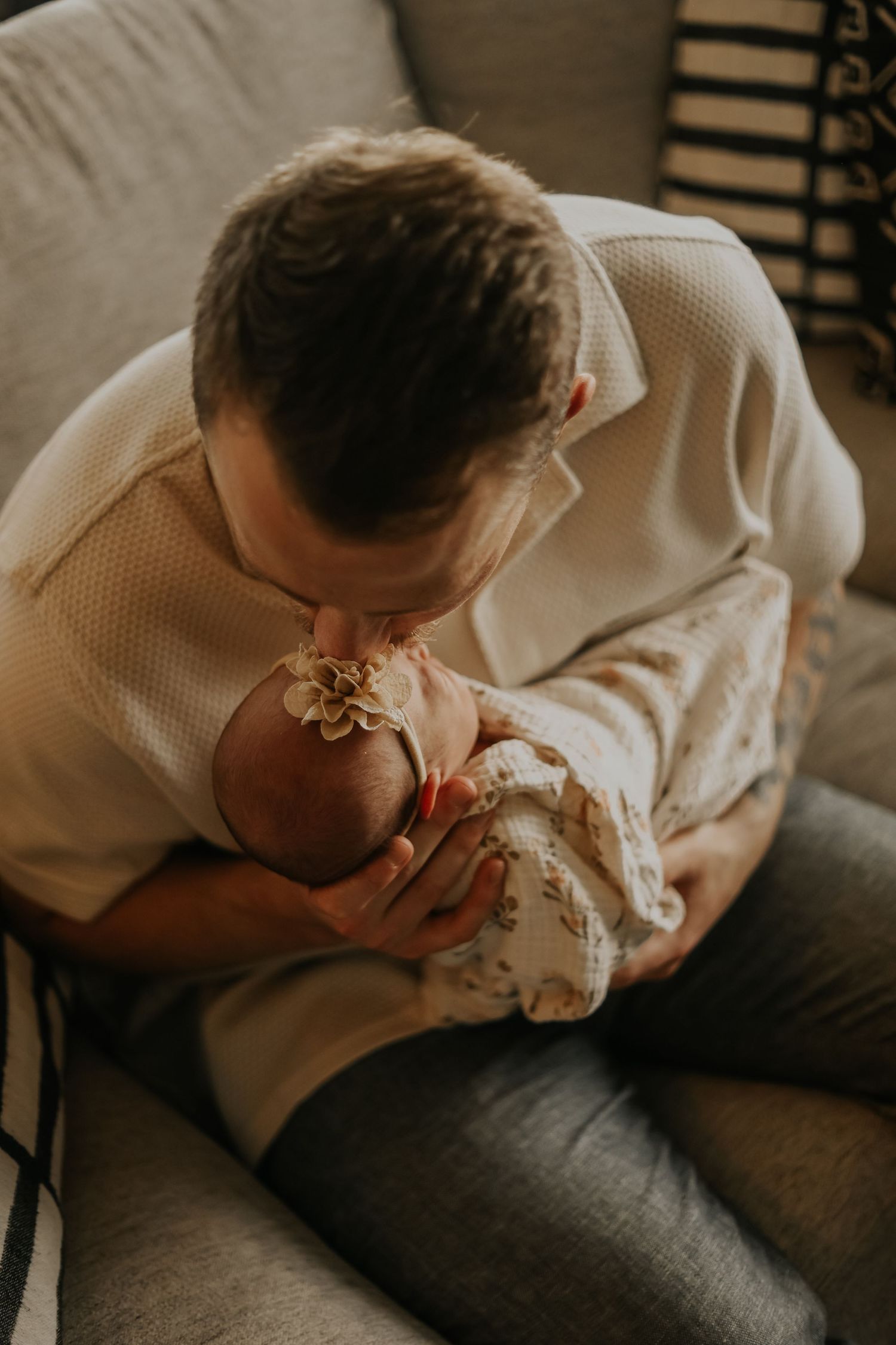 An intimate moment between parent and baby on a gray couch in warm lighting.