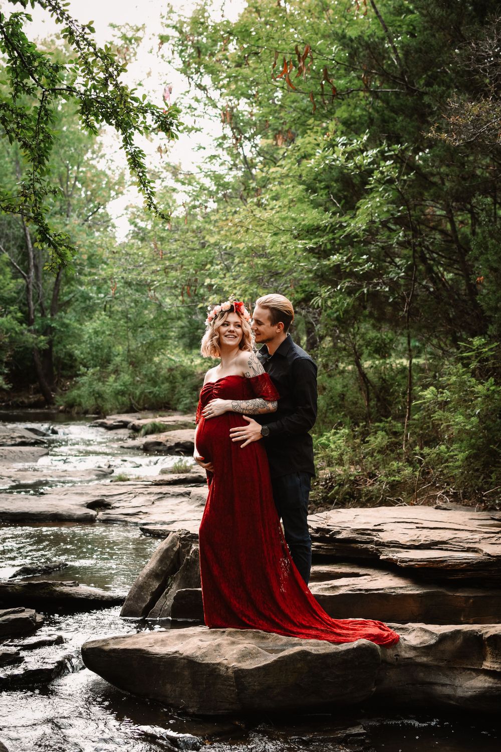 Maternity photography session in Dallas–Fort Worth featuring expecting mother in red flowing dress in rocky creek in Flower Mound, Texas