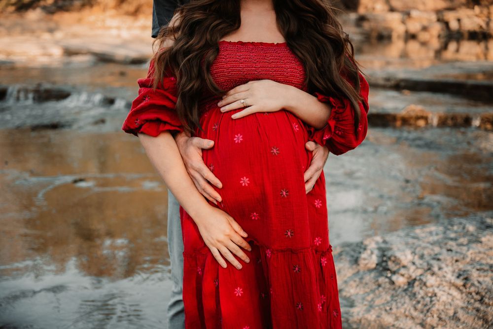 Couple holding pregnant belly during outdoor maternity photo session in DFW in the water