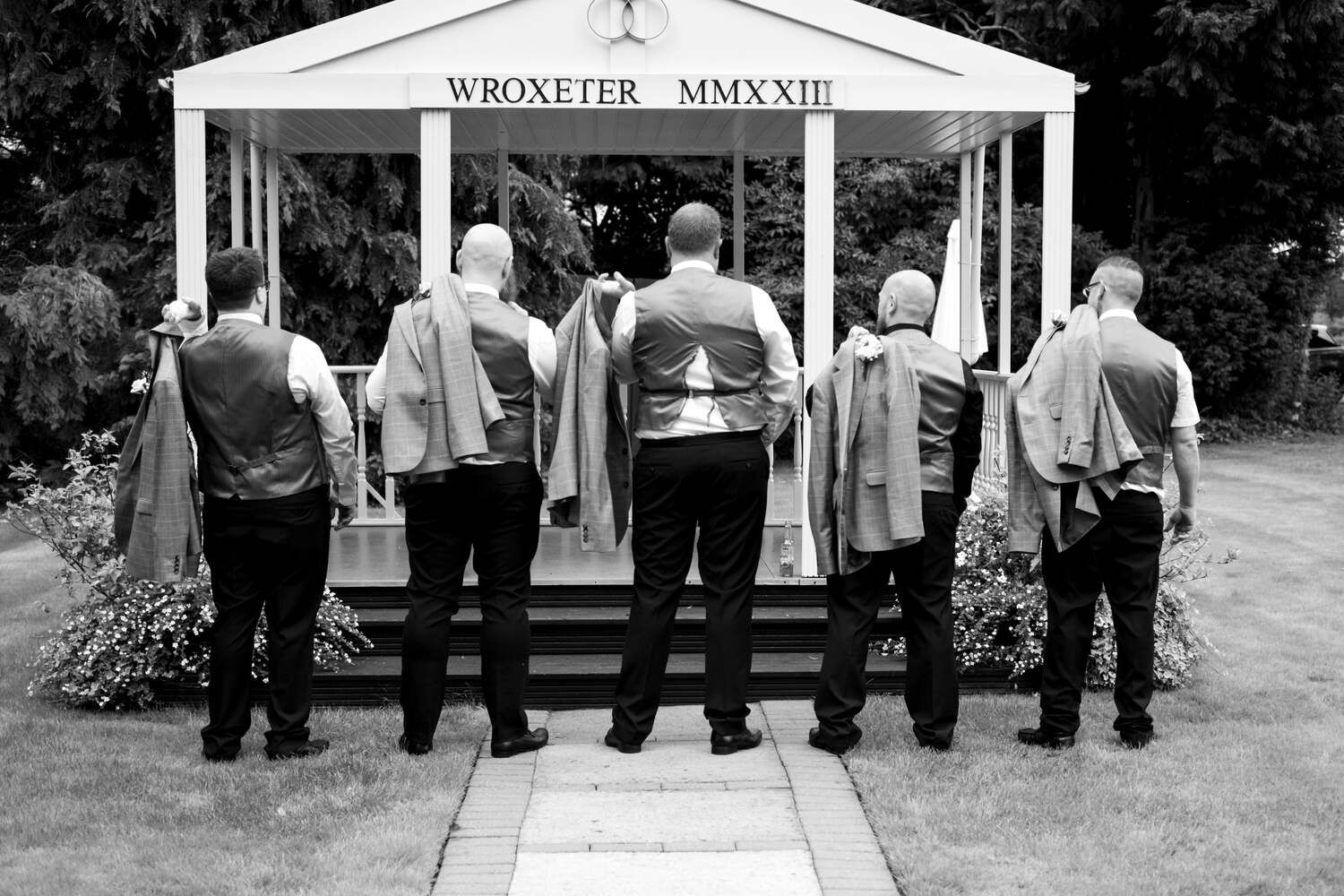 five groomsmen outside Wroxeter sign, middle grooms waistcoat is too small and split open