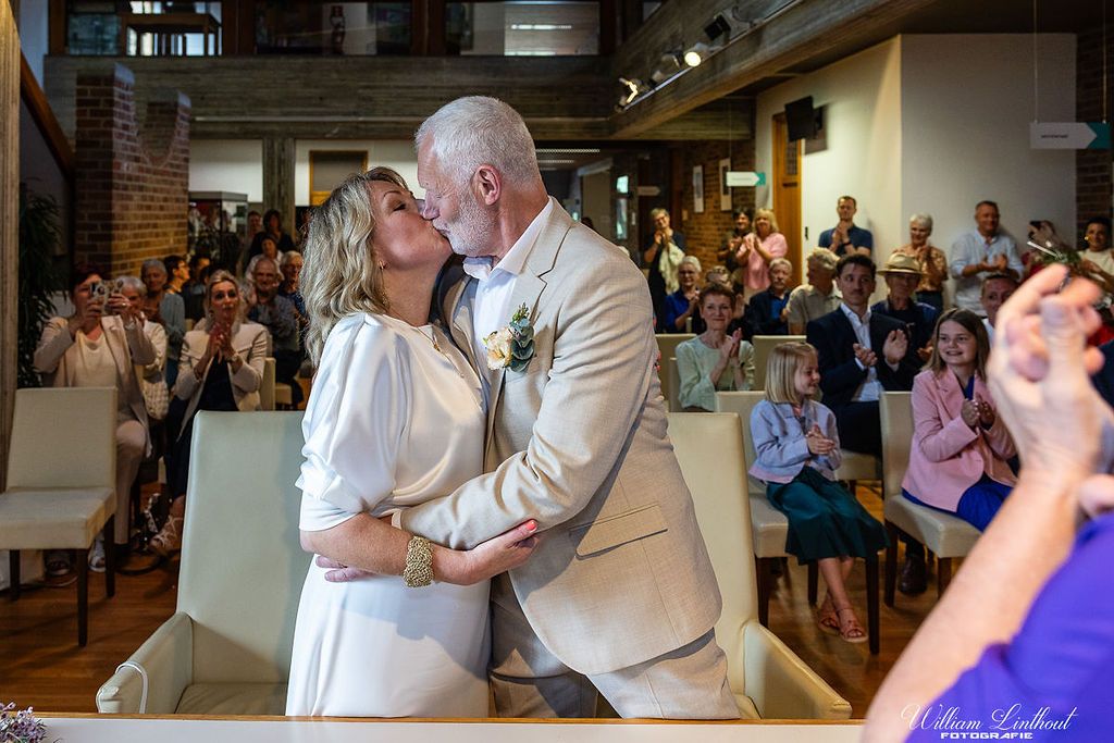 Wedding ceremony kiss moment in an industrial venue with exposed brick and gathered guests.