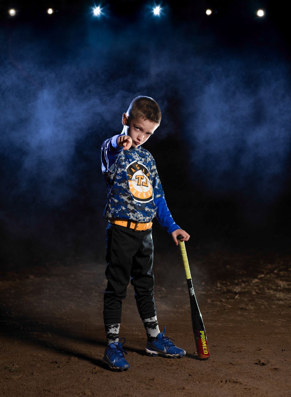 Young baseball player poses with bat in dramatic lighting with fog and stars in dark background.