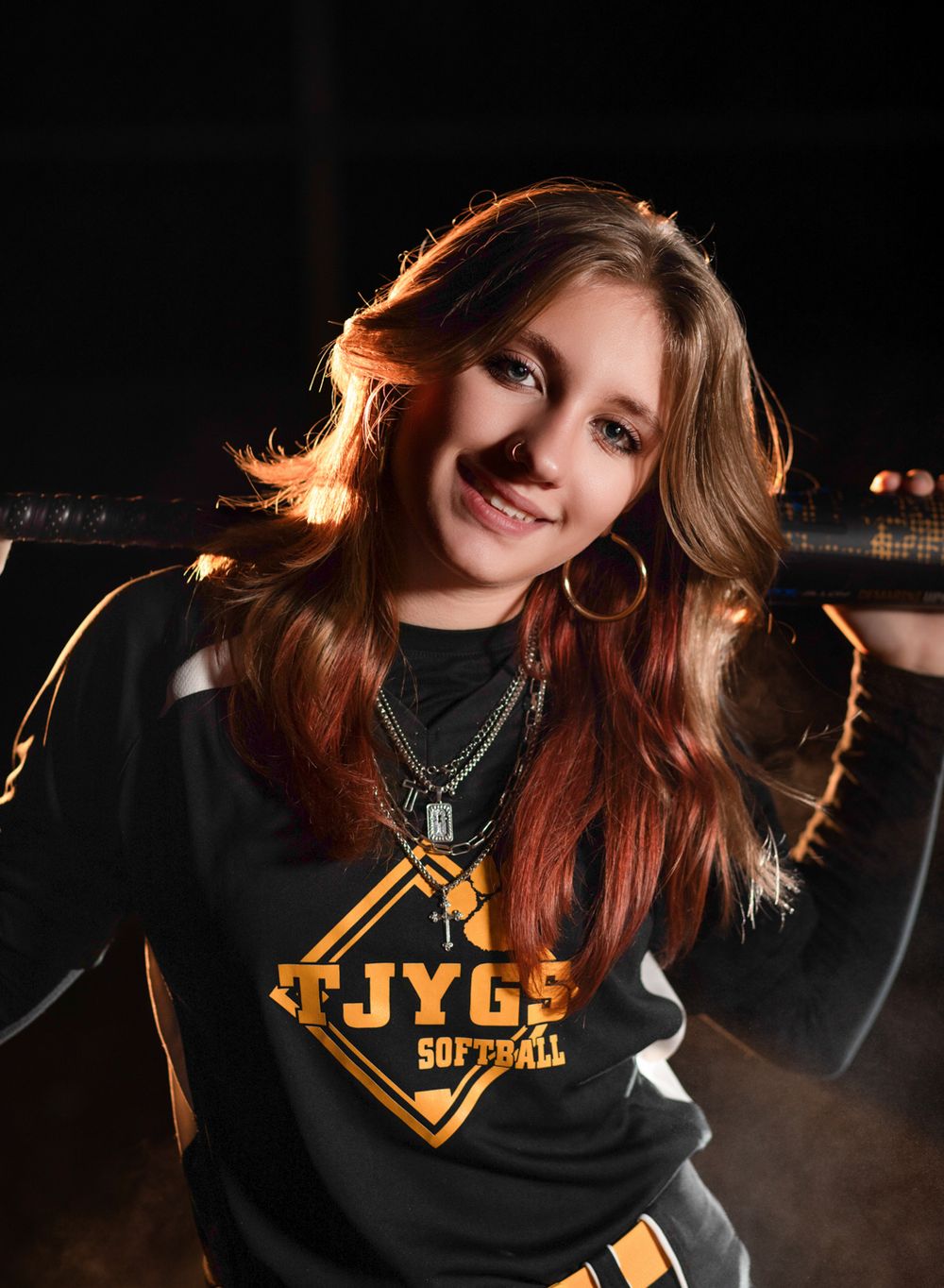 Portrait of an athlete in a black JYG softball team sweatshirt with rim lighting against dark background.