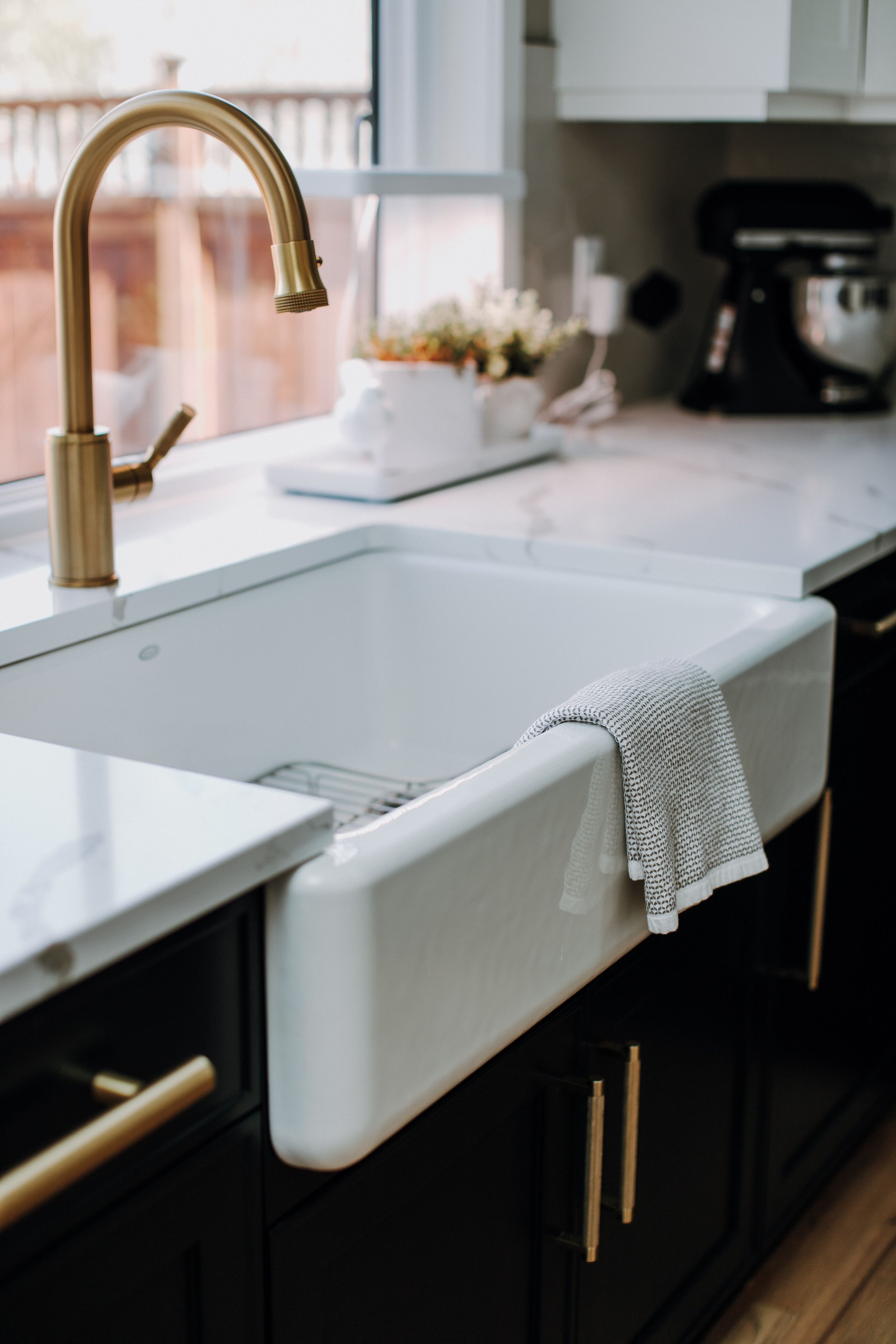 White farmhouse sink with brass faucet and black cabinets in modern kitchen design.