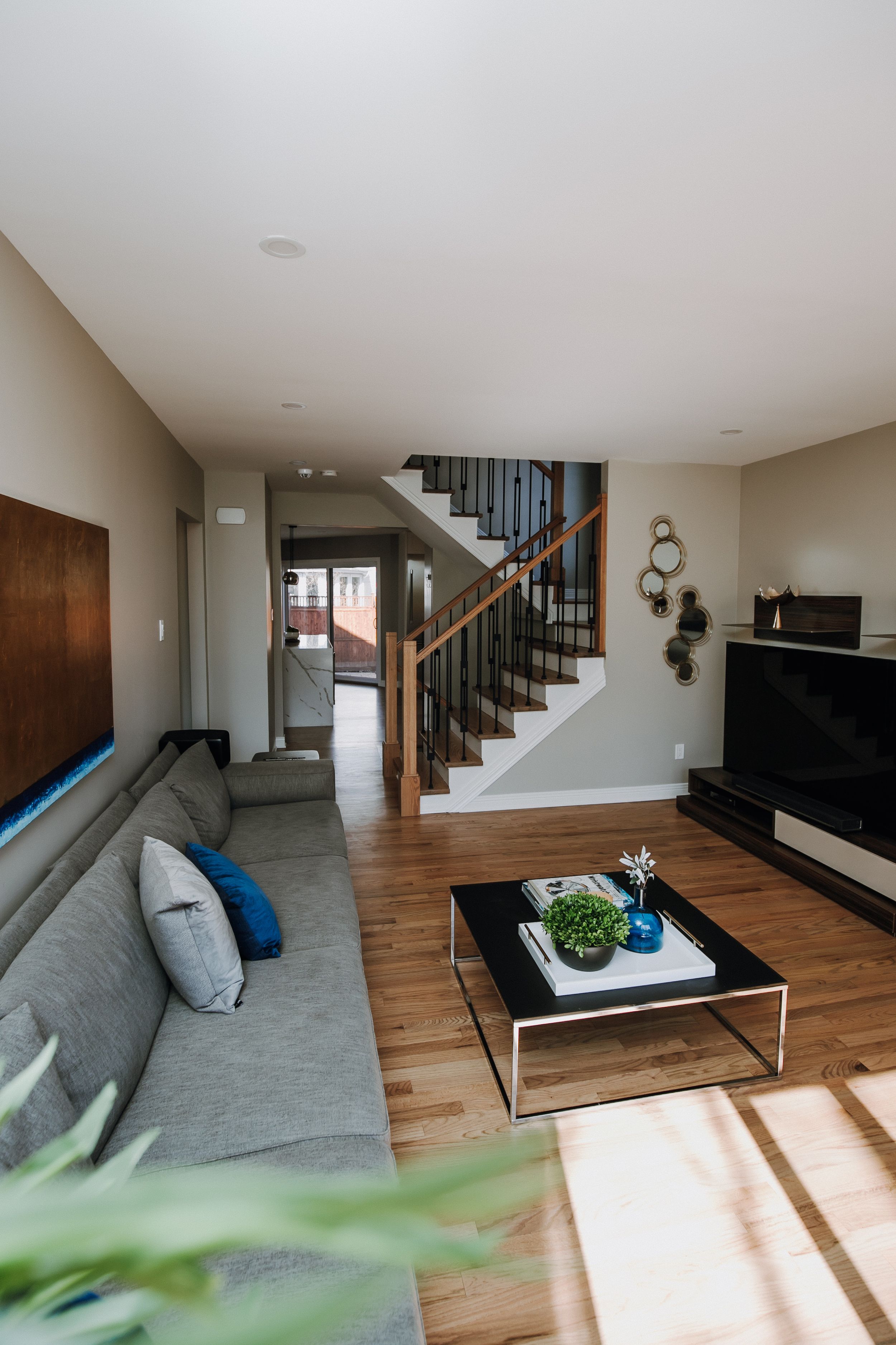 Contemporary living room with gray sectional, wooden stairs, and modern entertainment center.