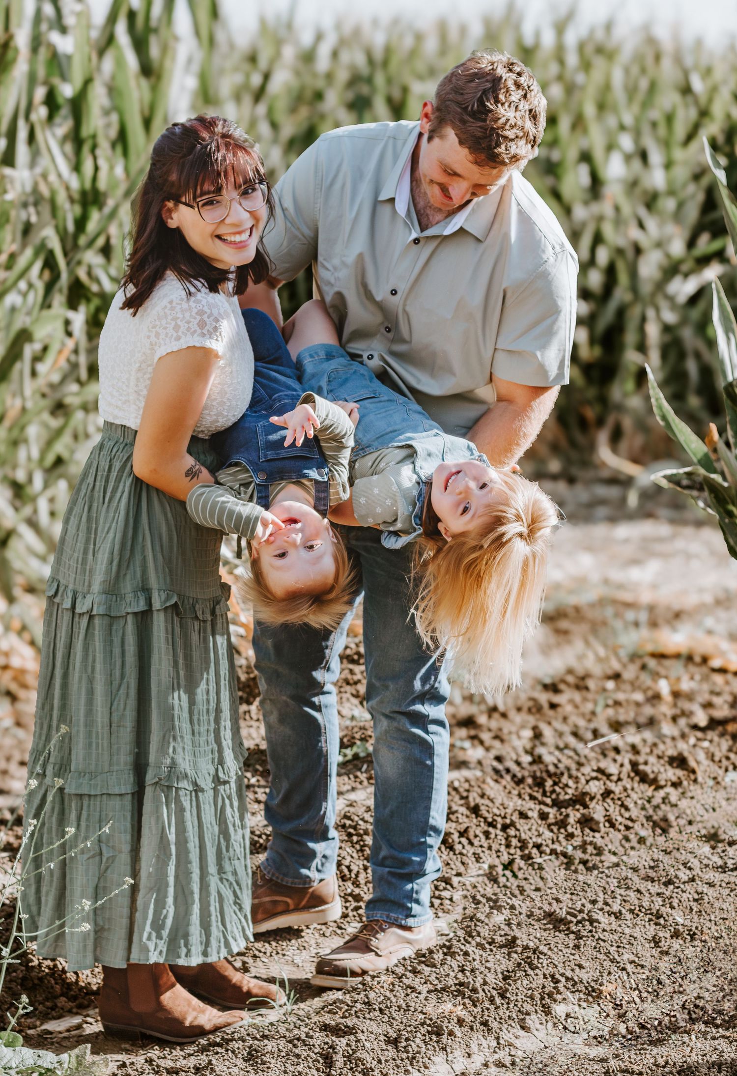 Playful family portrait in cornfield with children being held upside down. Fall mini photoshoot in Patterson, California.