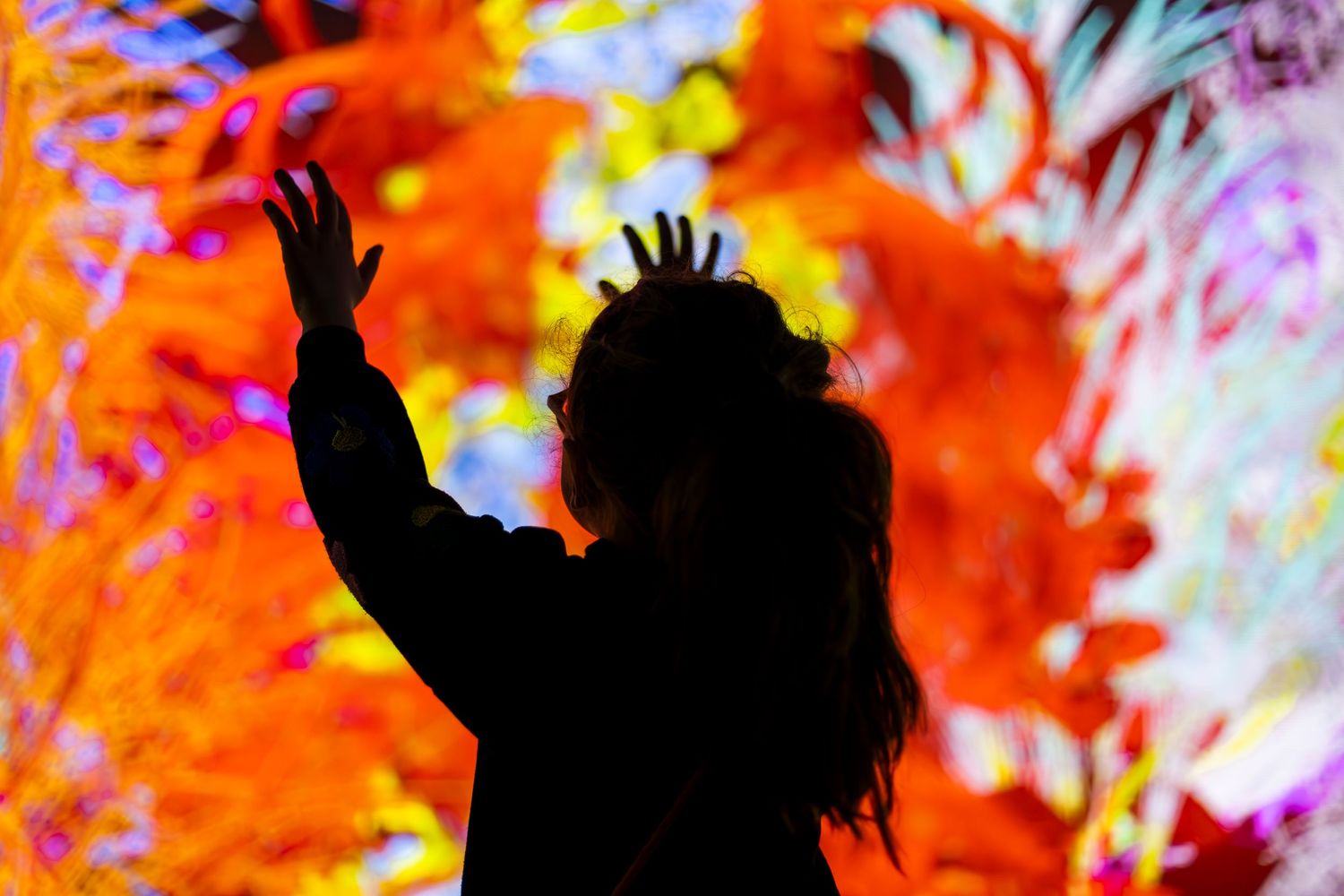 Silhouette of a person with raised arm against vibrant orange and multicolored psychedelic background.