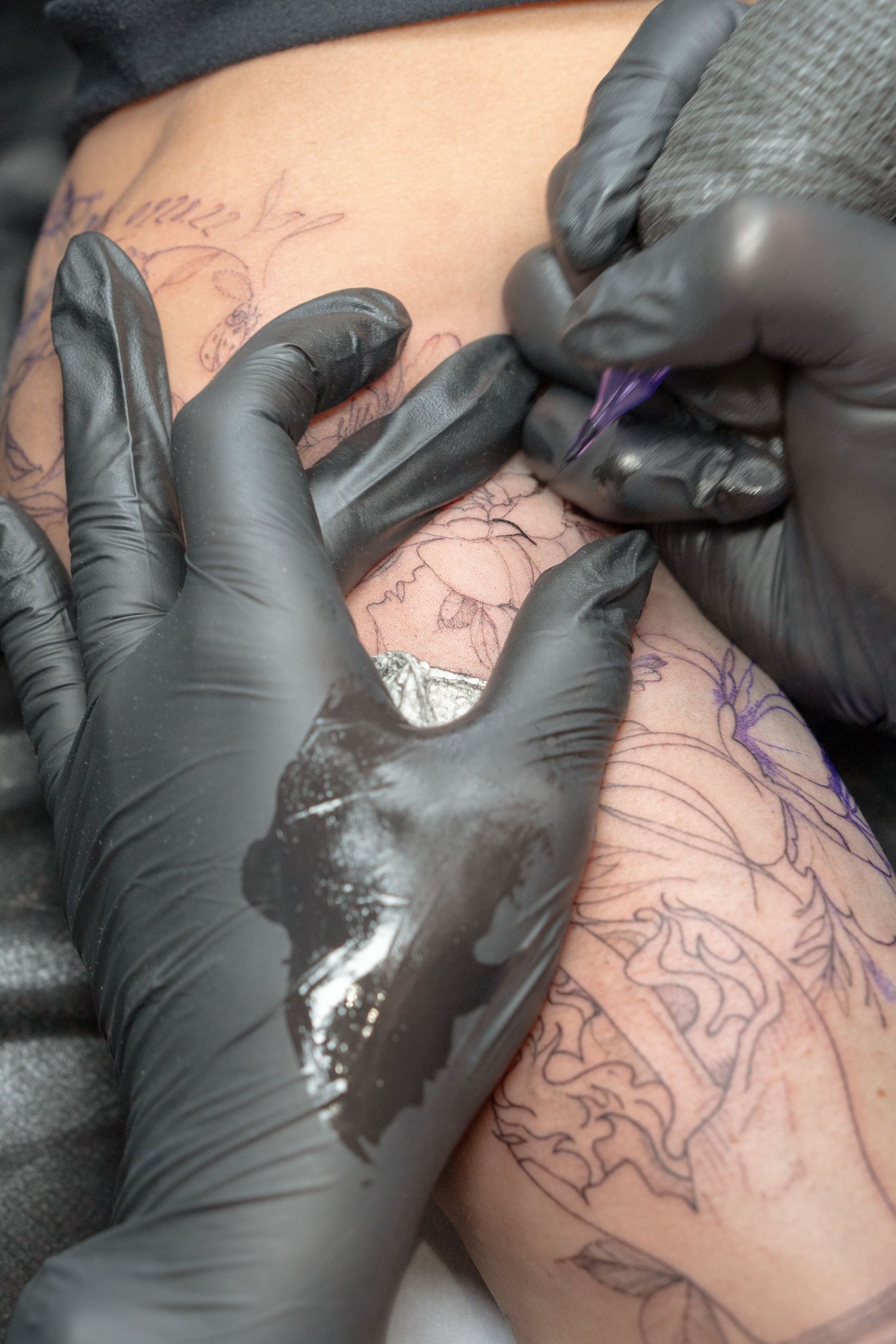 Tattoo artist using black gloves to create intricate line work on client's skin.