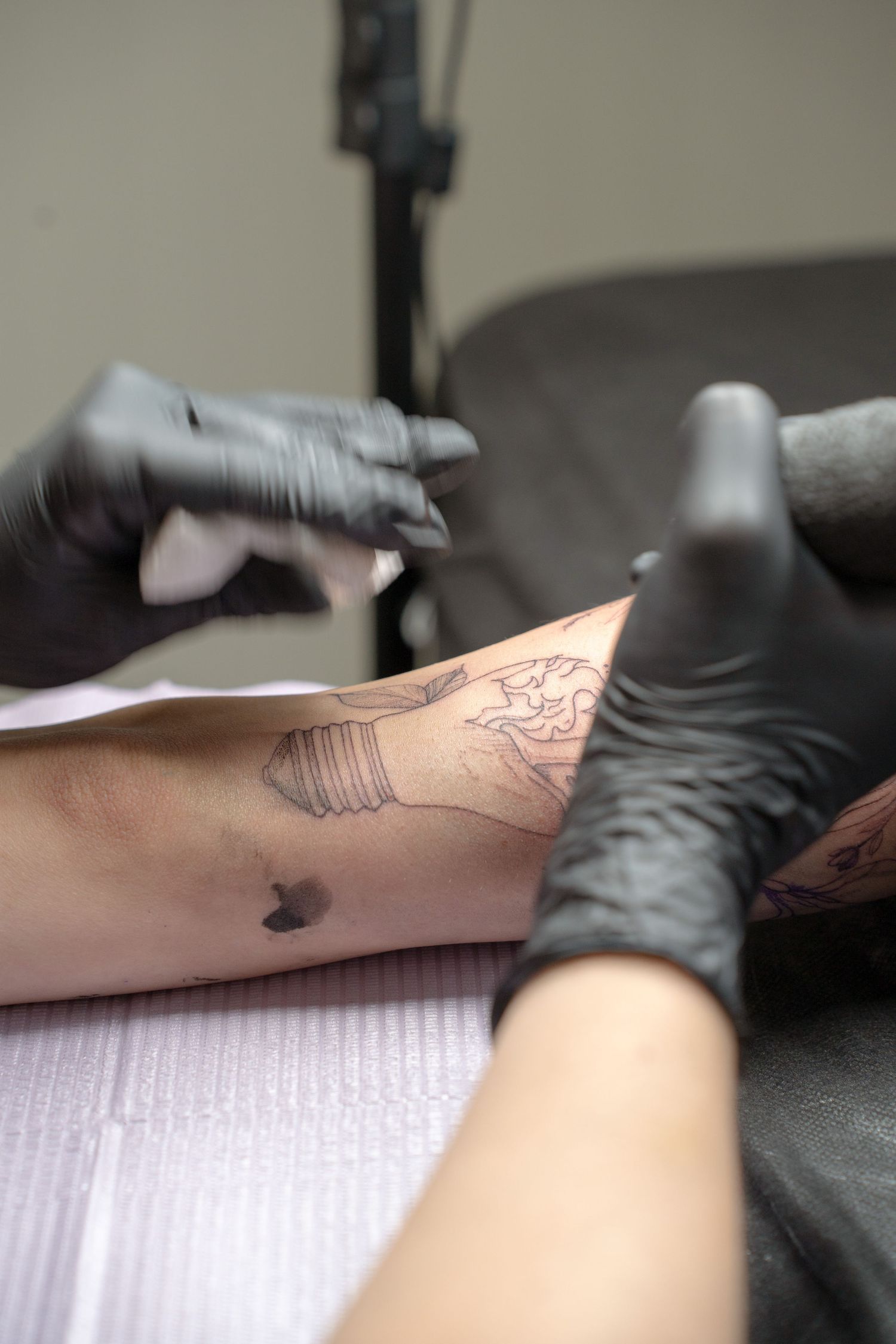 Close-up of hands in black gloves applying a detailed tattoo design on skin.