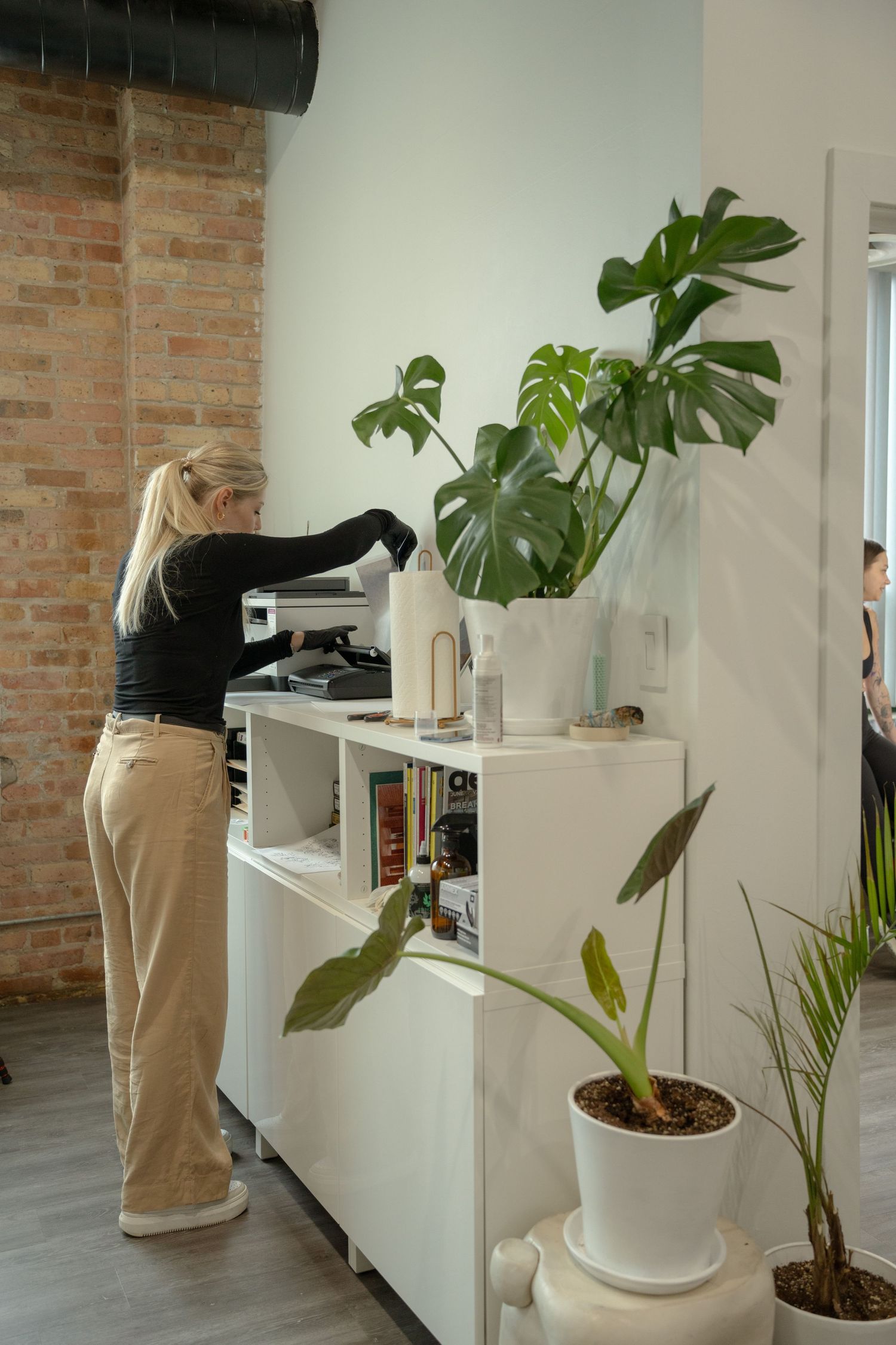 White cabinet workspace with monstera plant and office equipment against brick wall.
