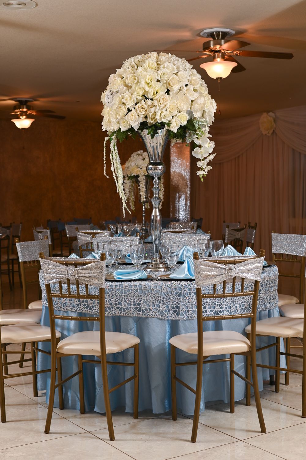 Elegant wedding reception table with tall white floral centerpiece and blue accents.