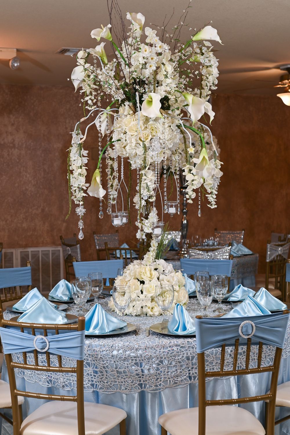 Tall crystal chandelier centerpiece with cascading white flowers on silver sequined table.
