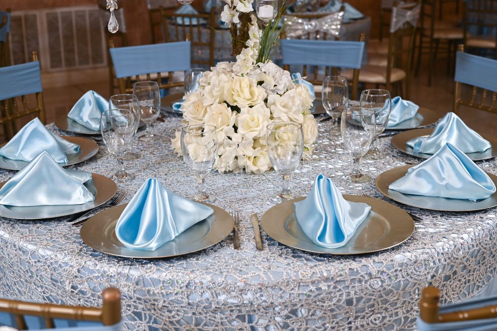 White floral centerpiece on sparkly tablecloth with light blue napkins and place settings.