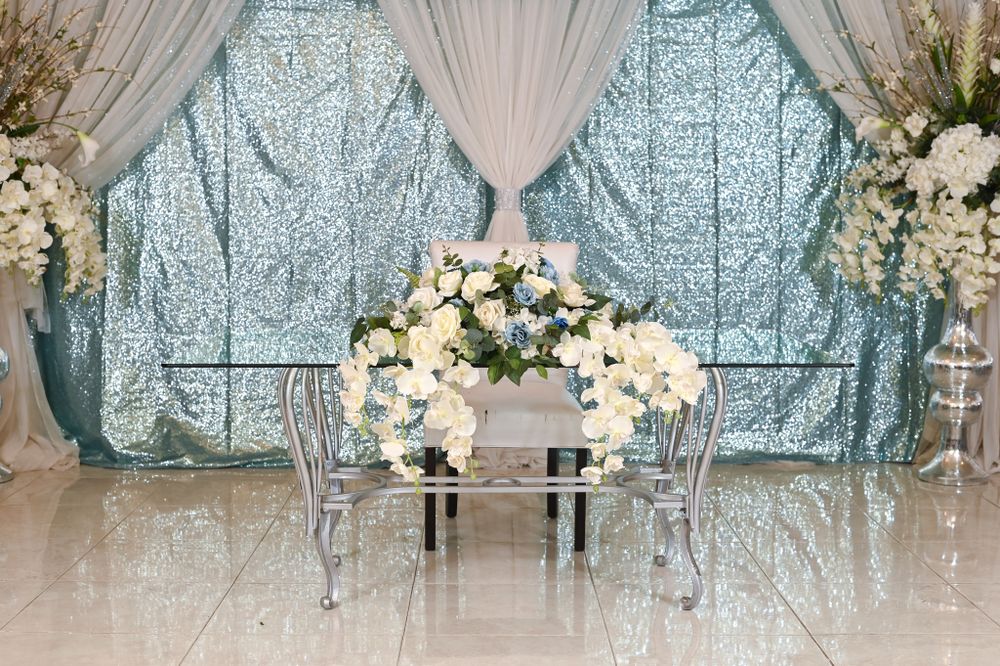 Elegant white floral arrangement with crystal chairs against draped window backdrop.