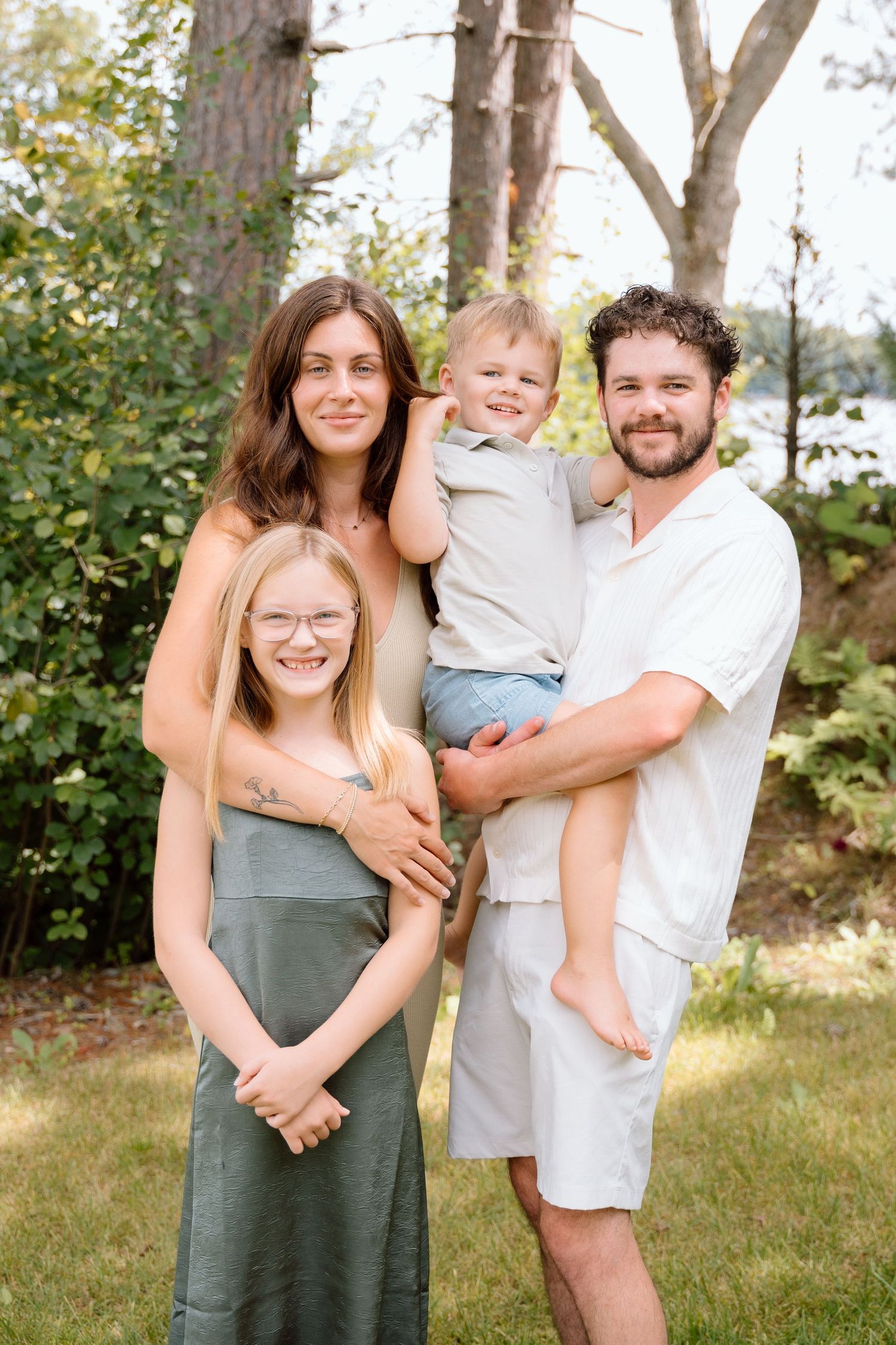 Family portrait outdoors with natural greenery and trees in background.