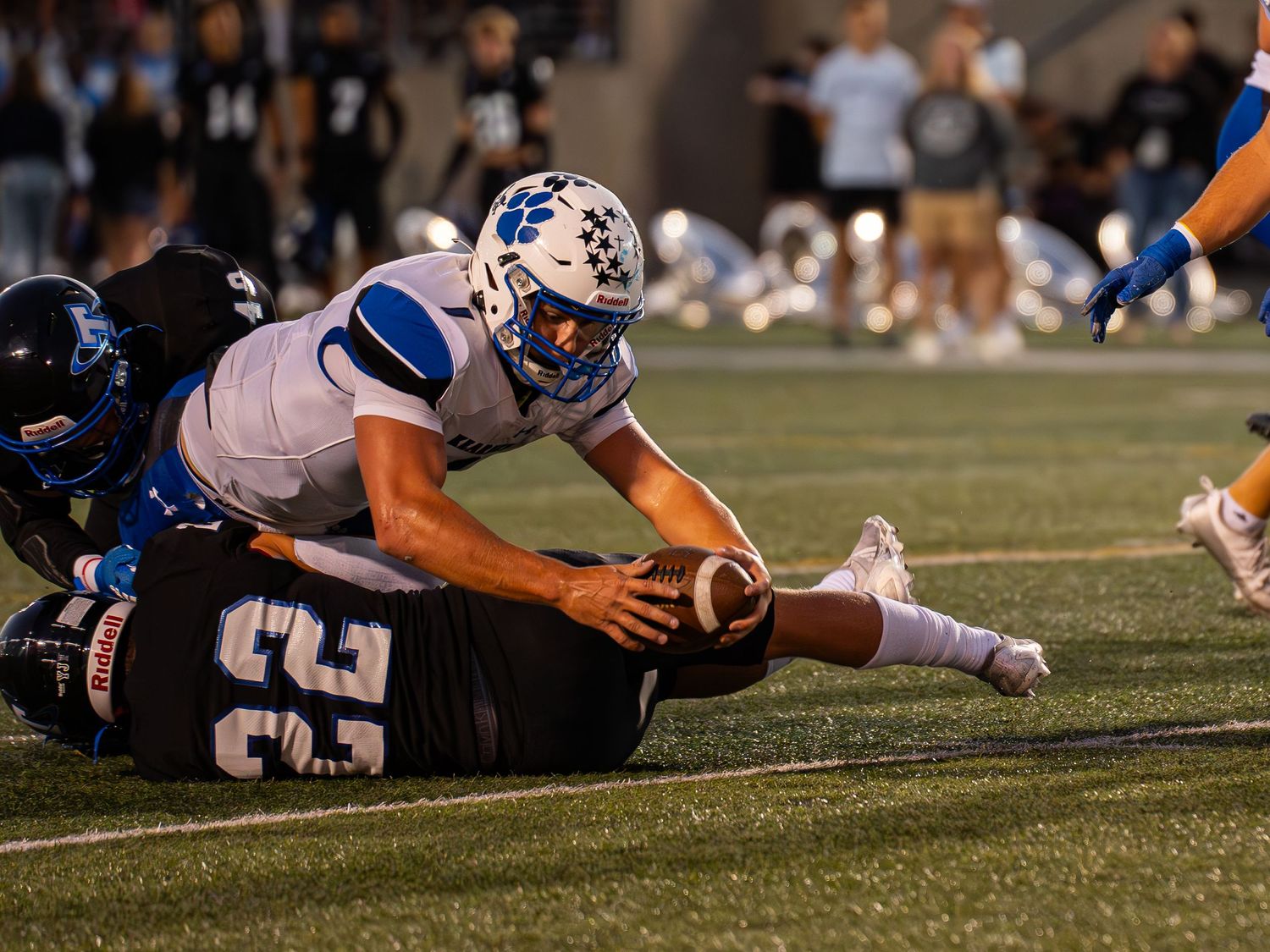 Football player stretches to secure the ball during intense ground play.