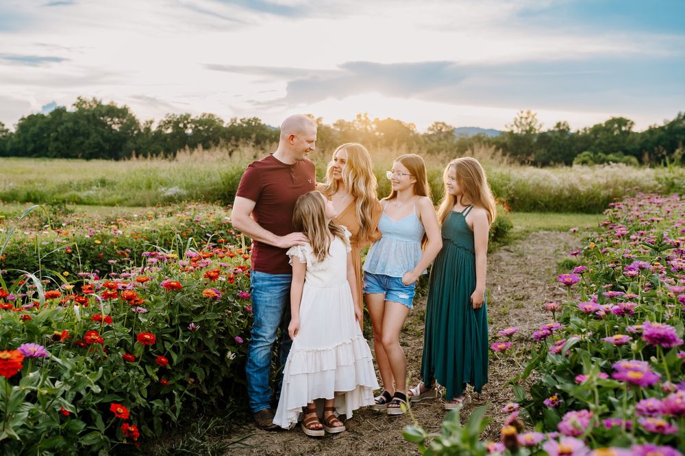 Family smiles at each other in zinnia field at golden hour