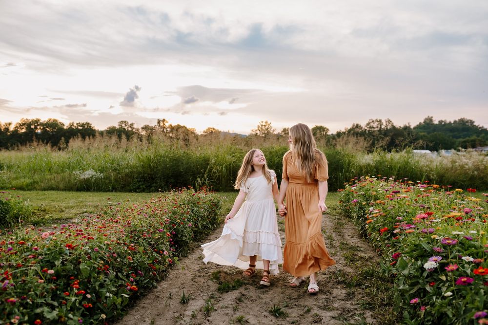Mom and daughter smile at each other as they walk hand in hand through zinnia field