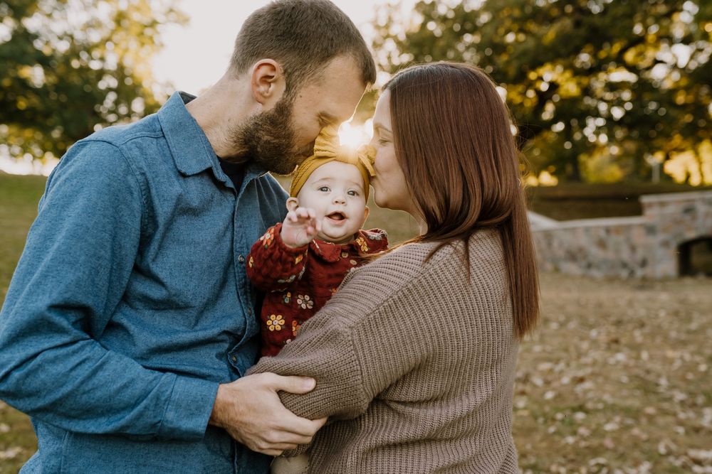 Parents color coordinated snuggle their baby girl at sunset for pictures in the park