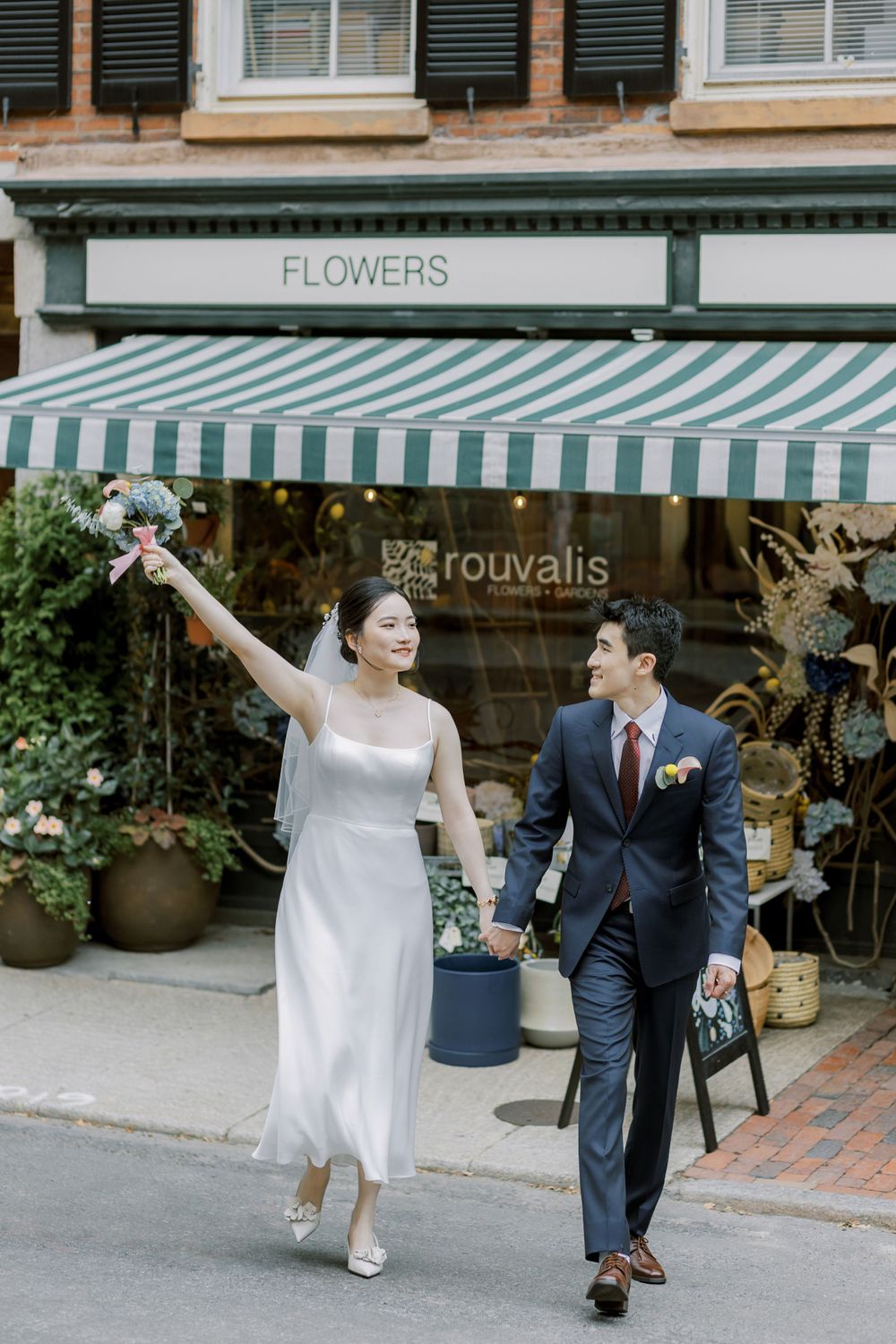 Celebratory moment outside a flower shop with striped awning and elegant wedding attire.