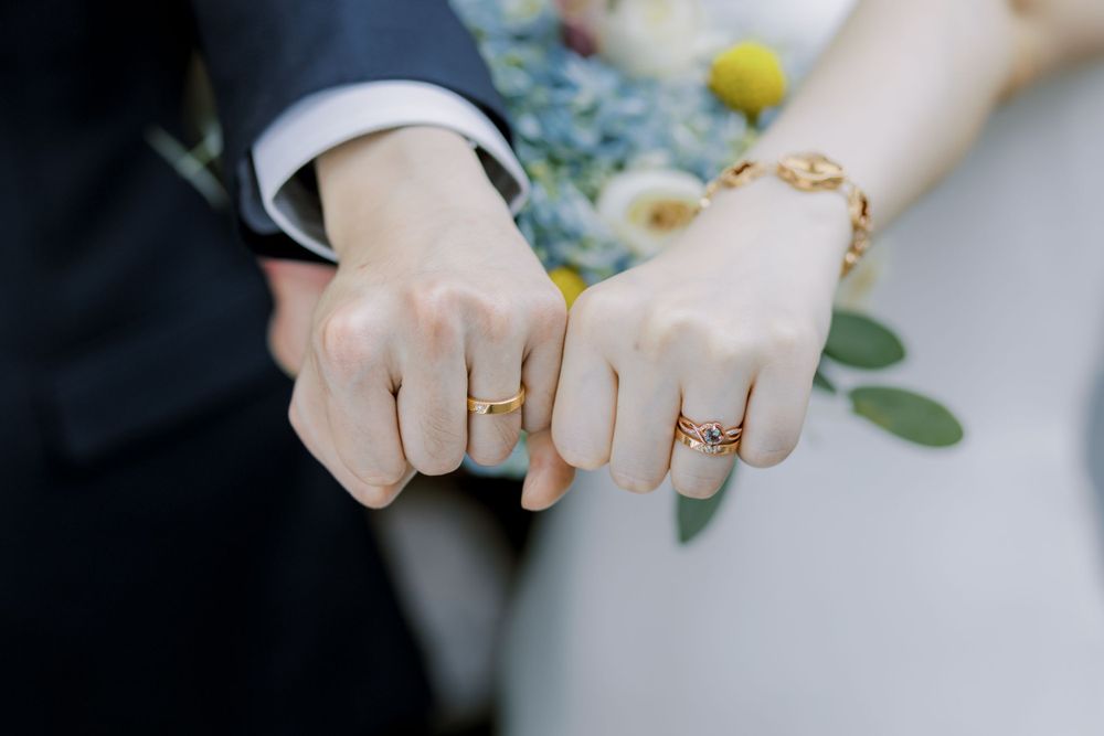 Close-up of wedding rings and hands against floral background.