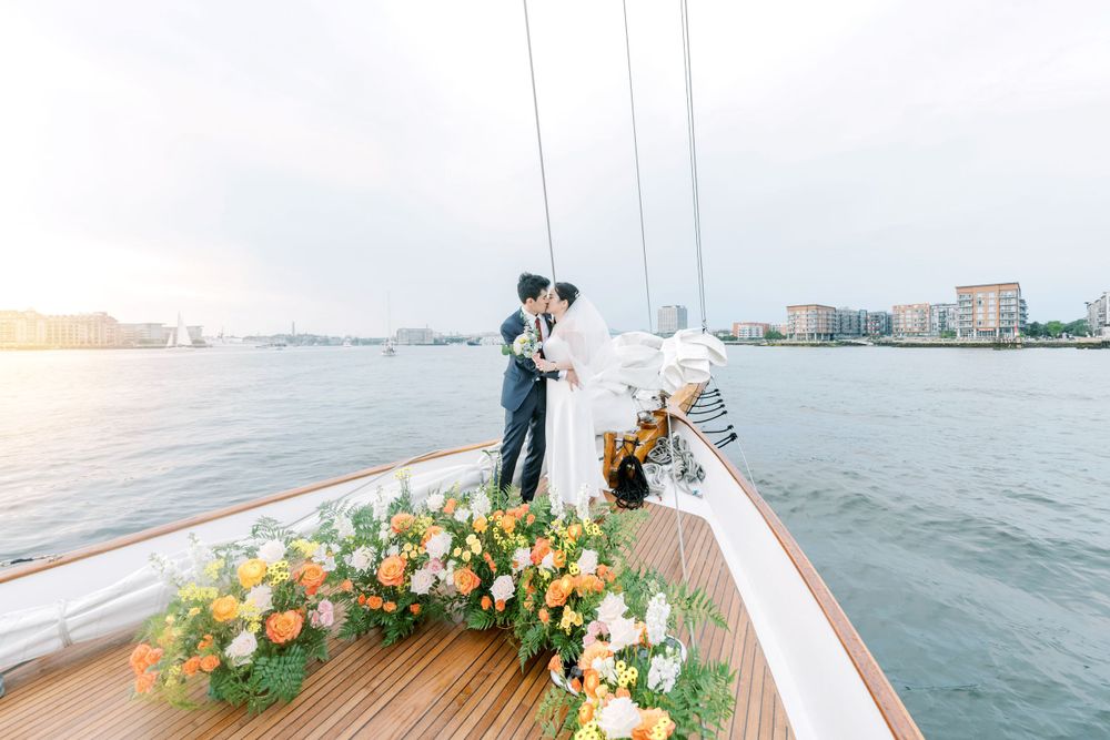 Wedding couple on a boat deck decorated with vibrant orange and white floral arrangements against a waterfront skyline.