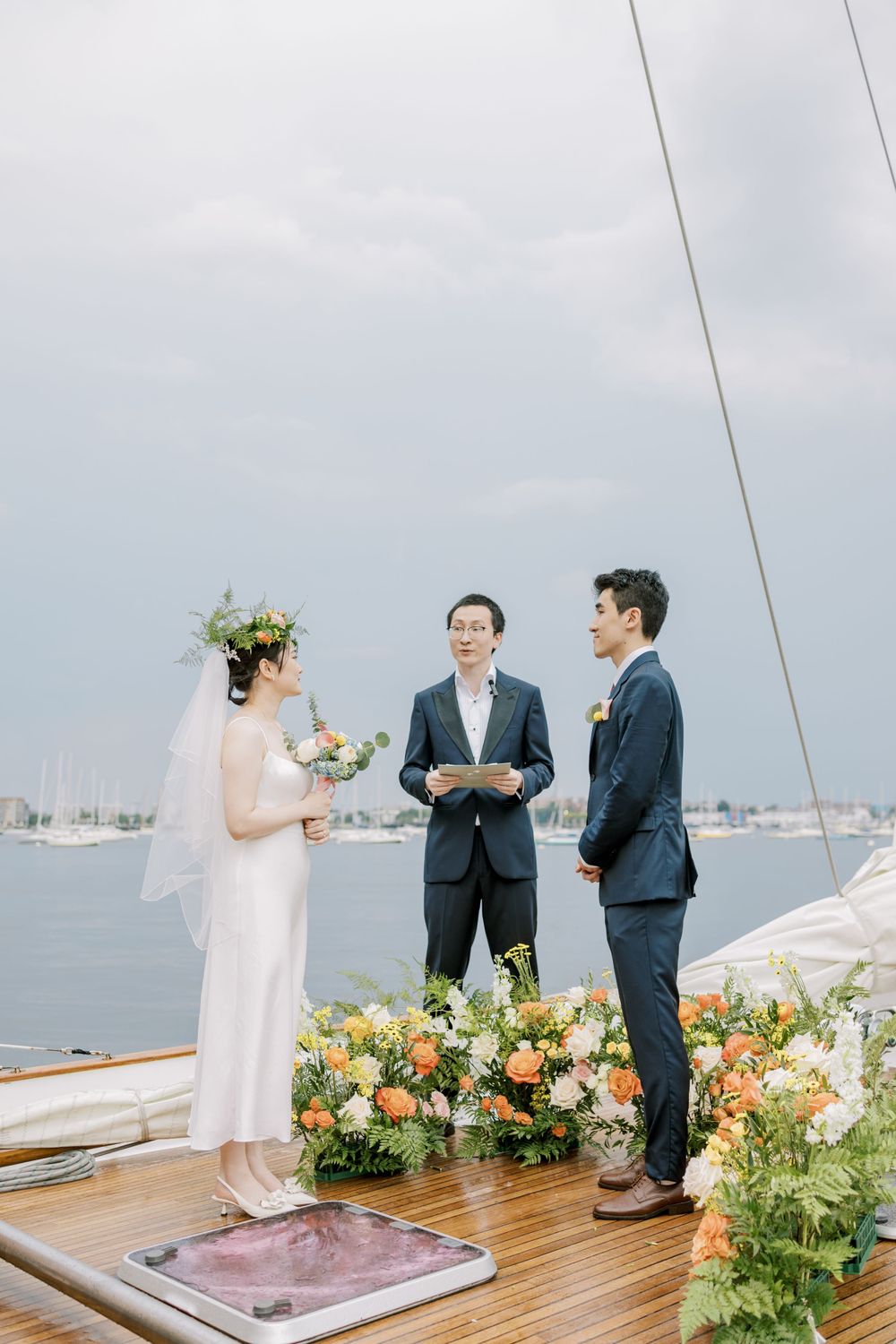 Wedding ceremony taking place on a boat deck with floral arrangements and harbor views.