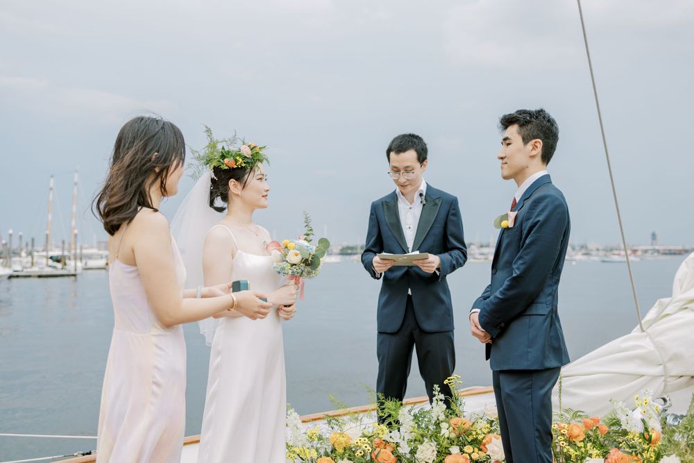 Intimate wedding ceremony on a boat with wedding party and officiant against harbor backdrop.