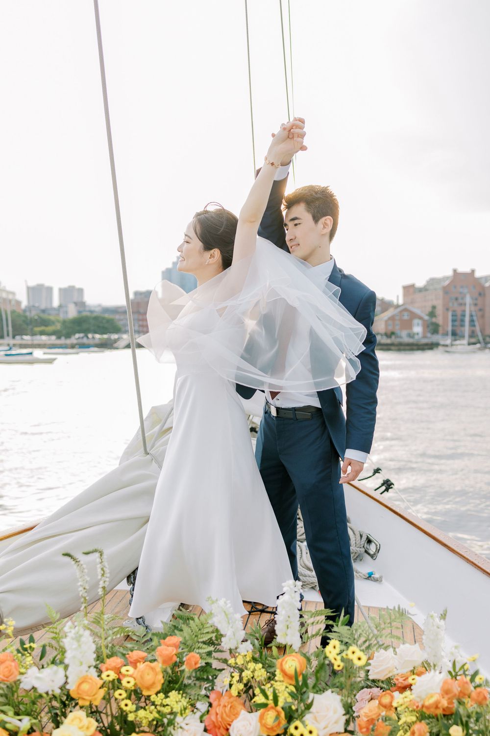 Joyful moment on a boat deck with flowing white dress and colorful floral arrangements.