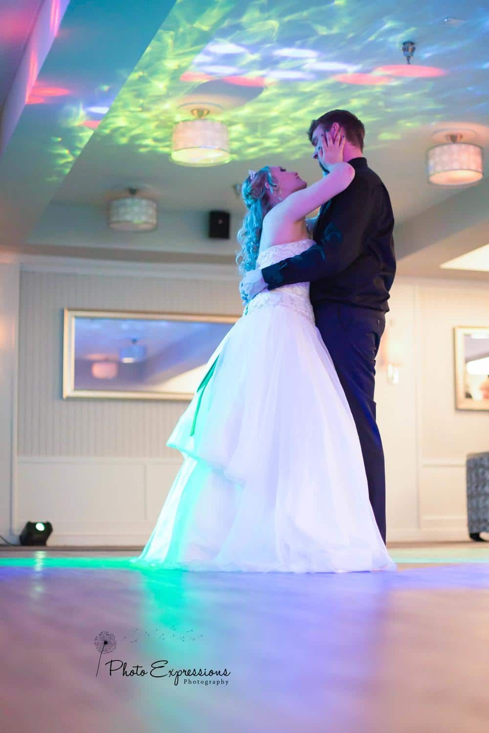 Wedding couple's first dance under colorful disco lights in reception venue.