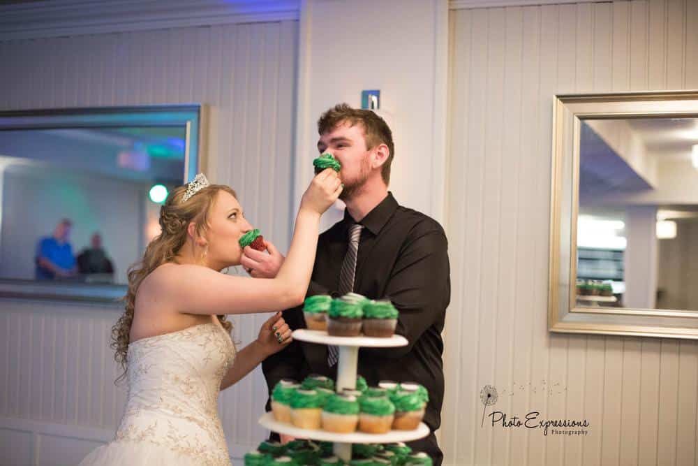 Wedding couple cutting green-frosted cupcakes at reception celebration.