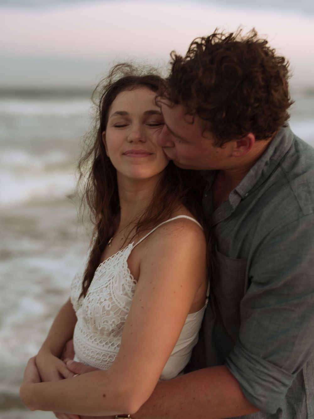 A romantic couple sharing an intimate moment on the beach at sunset, with waves crashing in the background.