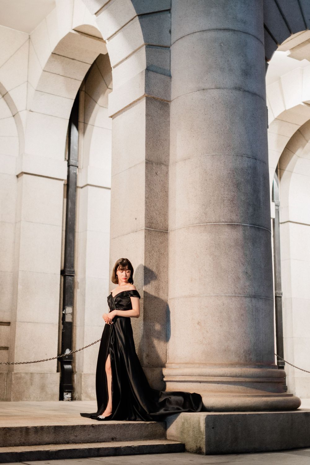 Woman in stunning black off-shoulder ball gown poses gracefully between grand stone columns.