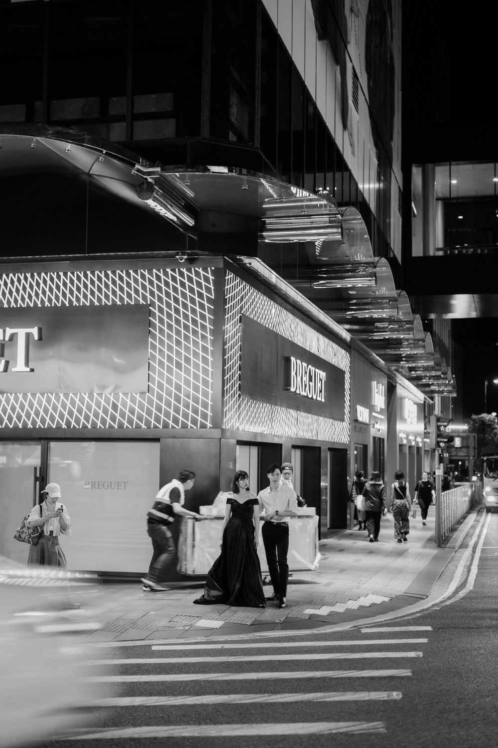 Couple in formal black and white attire posing on city street at night near Bvlgari store.
