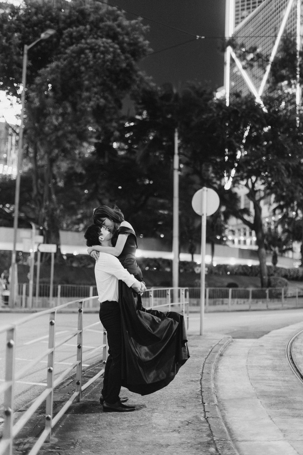 Romantic black and white photo of couple embracing on urban street at night, dress flowing.