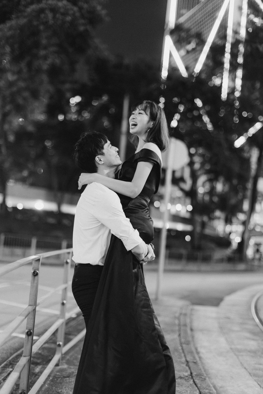 Black and white photo of a joyful couple embracing and laughing together at night near a ferris wheel.