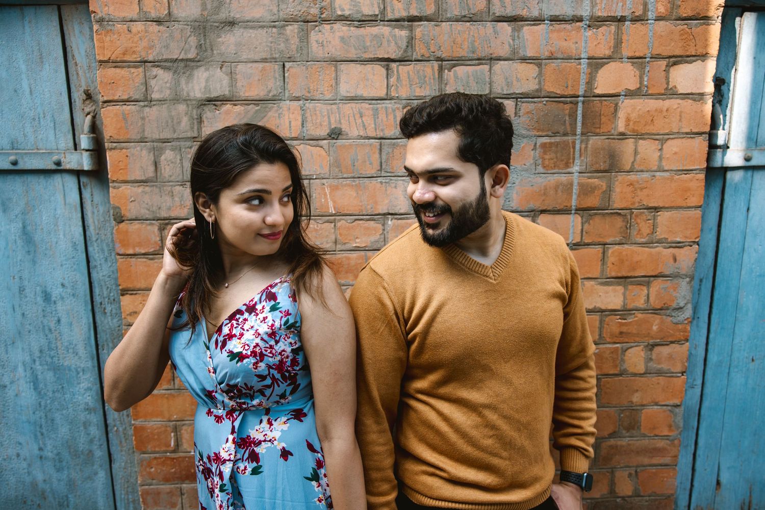 A couple poses against a rustic brick wall background in a casual photoshoot setting.