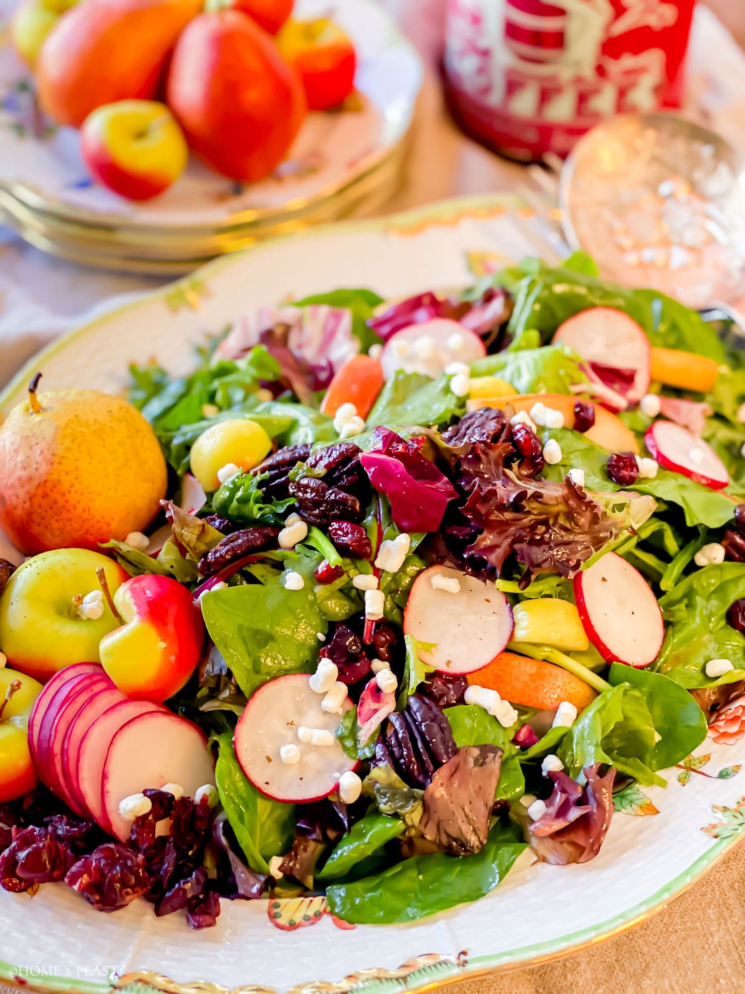 Fresh garden salad with sliced fruits, mixed greens and dried cranberries on an ornate plate.
