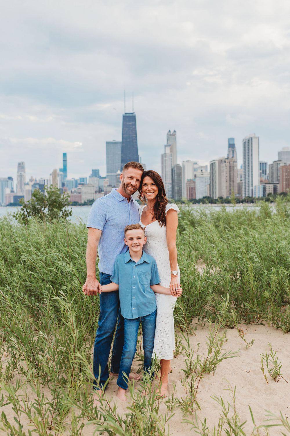 Family poses together in beach grass with Chicago skyline in background.