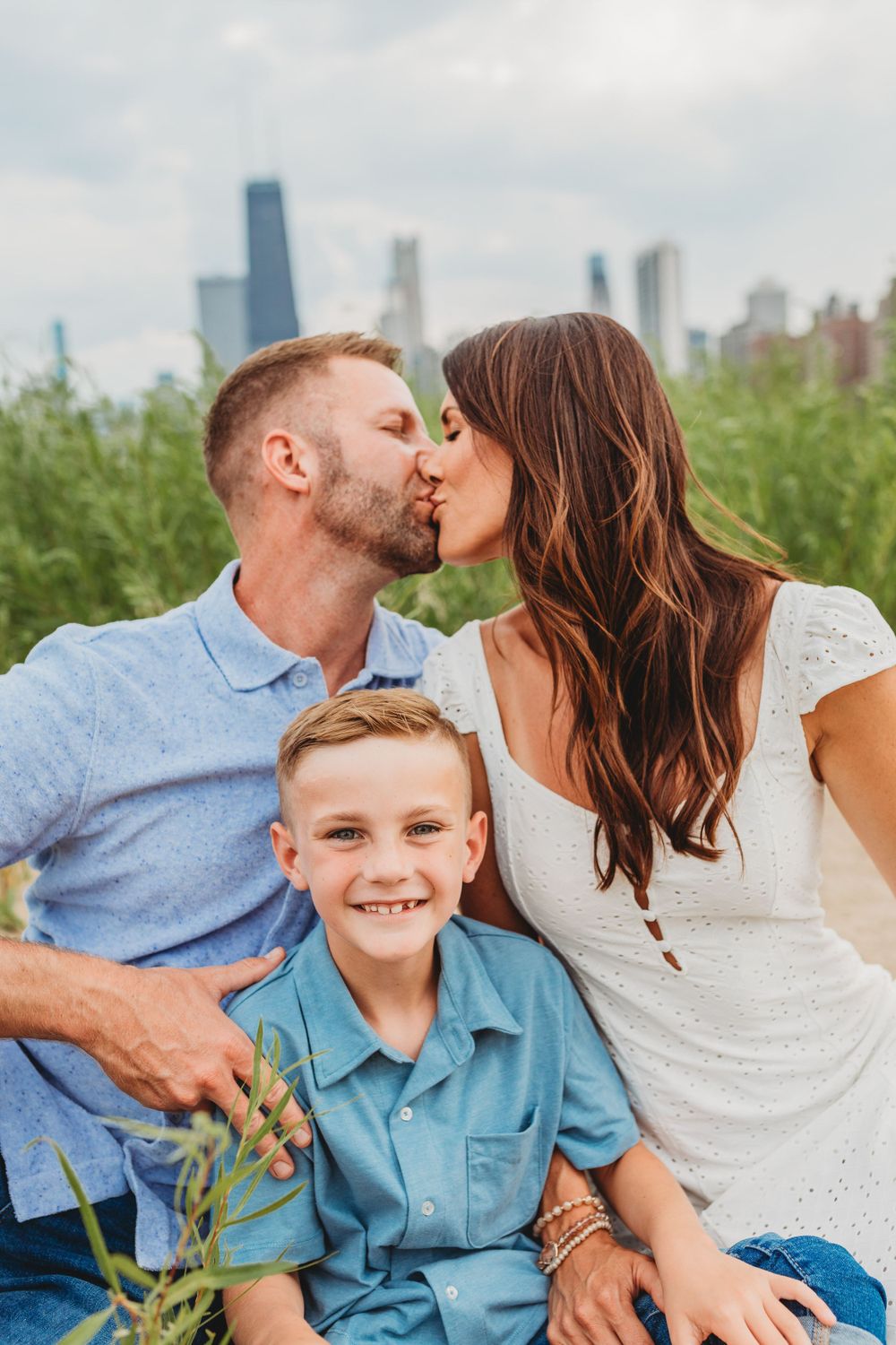 Casual family portrait among beach grass with urban skyline visible in distance.