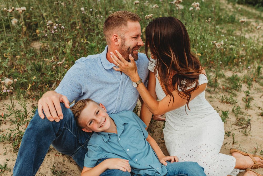 Relaxed family poses on beach dunes during summer photo session.